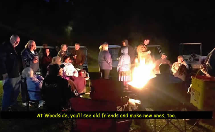 Color photo of men and women standing around campfire at night. 